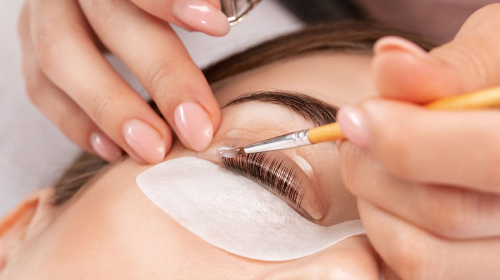 Make-up artist makes the procedure of lamination and dyeing of eyelashes to a beautiful woman in a beauty salon. Eyelash extensions. Eyelashes close-up